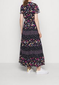 Maxiklänning med korta ärmar, svart tyg med färgglada blommönster och lagerdesign, bärs med vita sneakers med guldaccent.