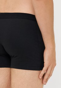 Černé bavlněné boxerky s elastickým pasem, přiléhavým střihem a plochými švy, které zdůrazňují hladký povrch a minimální detaily.