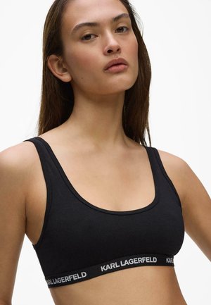 Donna che indossa un reggiseno sportivo nero Karl Lagerfeld con scollo a U su sfondo bianco.