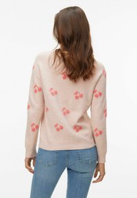 Jasnoróżowy sweter o miękkiej fakturze, ozdobiony czerwonymi wzorami wiśni. Ściągacze na mankietach i dole, dekolt w kształcie okrągłego kołnierza. Noszony z niebieskimi dżinsami.
