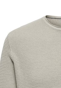 Helle graue Strickjacke mit strukturiertem Muster, Rundhalsausschnitt und gerippten Details am Kragen, die eine weiche, gewebte Textur präsentiert.