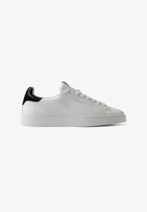 Sneaker en cuir blanc avec un accent noir au talon, semelle en caoutchouc plate et fermeture à lacets à cinq œillets. Surface lisse et design minimaliste.