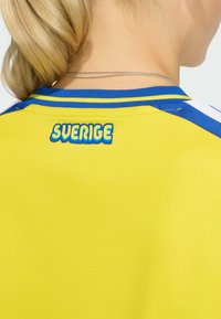 Gelbes Sporttrikot mit blauen Akzenten und dem Schriftzug "SVERIGE" auf der Rückseite. Der Stoff ist glatt, mit einem Rundhalsausschnitt und kontrastierenden Streifen.