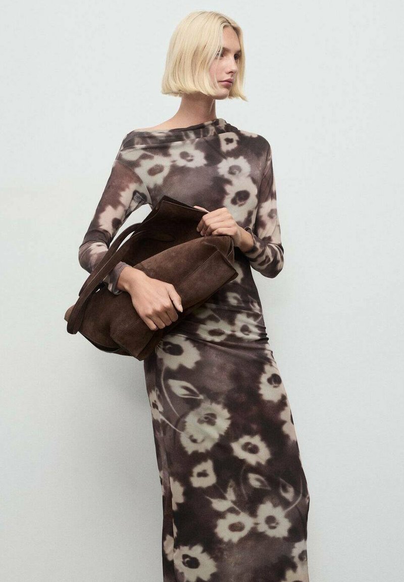 Rochie cu mânecă lungă, cu un model floral în nuanțe de maro, negru și crem. Modelul ține o geantă din suede maro închis. Textură netedă, siluetă ajustată.