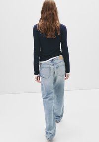 Jeans de mezclilla azul de cintura alta con un corte relajado, lavado claro y bolsillos traseros. Combinados con una camiseta ajustada de manga larga en color marino.