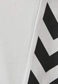 Hvidt stof med en struktureret overflade, der har dristige sorte chevronmønstre. Designet skaber en kontrast og visuel interesse.