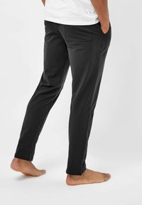 Zwarte, slim-fit broek van zachte stof, met zijzakken en een subtiele naaddetail. Draag met blote voeten.