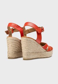 Sandales compensées en cuir rouge avec talons en jute tressé, dotées d'une bride cheville réglable et d'un design découpé pour la respirabilité.