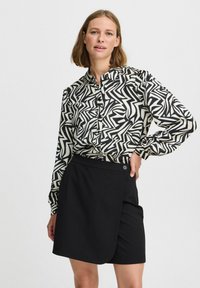 Gonna nera a portafoglio con chiusura a bottone abbinata a una camicia a maniche lunghe con un motivo astratto in nero e crema.