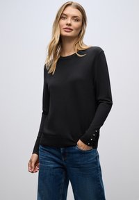Maglione nero a maniche lunghe in maglia liscia con scollatura a girocollo e dettagli in bottone sui polsini, abbinato a jeans di denim blu.