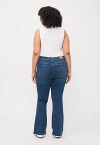 Jeans de mezclilla azul acampanados con una cintura de altura media, bolsillos traseros y una textura suave, combinados con una blusa sin mangas blanca.