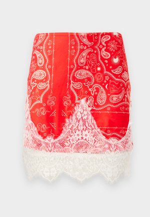 Mini gonna rossa con stampe a paisley bianche e motivi mistici, rifinita con pizzo floreale bianco all'orlo.