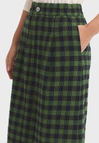 Falda a cuadros verde y azul marino con cinturilla elástica, bolsillos laterales y tejido texturizado. Presenta un detalle decorativo de botón.