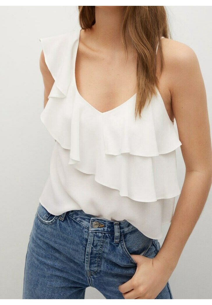 Femme portant un chemisier blanc sans manches à volants, rentré dans un jean bleu taille haute, avec une main dans la poche.