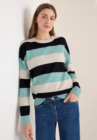 Sweter w paski w kolorach teal, granatowym i beżowym, z okrągłym dekoltem i ściągaczami, połączony z dżinsami. Gładka struktura dzianiny.