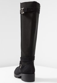 Botas negras hasta la rodilla con una sección inferior de ante y una parte superior de tela texturizada, con un detalle de hebilla y un tacón grueso.