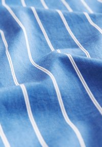 Blauer Stoff mit glatter Textur und vertikalen weißen Streifen. Das Material wirkt leicht und fällt weich.