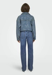 Chaqueta de denim con un diseño azul desgastado, que presenta intrincados patrones de costura blanca. Combinada con jeans azules de pierna recta y cintura alta.