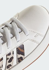 White leather sneaker with gray laces, featuring leopard print accents on the side and a smooth rounded toe. Rubber sole.