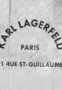 Silver textured material featuring bold black lettering. Text includes "KARL LAGERFELD," "PARIS," and "1 RUE ST-GUILLAUME."