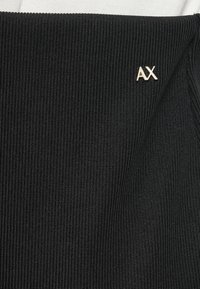 Μαύρο υφασμάτινο ριμπ με υφή, που διαθέτει μια χρυσή λεπτομέρεια με το λογότυπο "AX" στο πλάι. Το προϊόν έχει έναν λείο και εφαρμοστό σχεδιασμό.