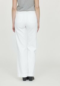 Pantalons larges blancs en tissu léger,dotés de poches arrière et d'un ourlet net, associés à un haut gris ajusté et des chaussures noires.