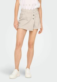 Beige denim nederdel med en knaplukning foran, bæltesløjfer, to sidelommer og en let A-formet snit, parret med hvide sneakers.