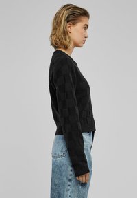 Zwarte gebreide trui met een dambordstructuur, ronde hals en geribbelde zoom. Gepaard met lichtblauwe gewassen denim jeans.