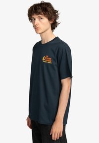 Navy blue cotton t-shirt with short sleeves, featuring a printed logo in orange on the chest. Classic crew neckline, relaxed fit.