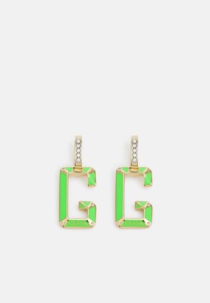 Boucles d’oreilles en forme de "G" dorées et vert néon avec des pierres transparentes sur les crochets et le mot "GUESS" gravé en bas.