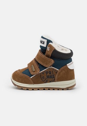 Brown and navy blue ankle boots with velcro straps. Suede and fabric materials, textured surface, white accents, rubber sole with grip.