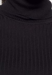 Pull à col roulé noir en maille côtelée, doté d'un col montant et d'une surface texturée, conçu pour un ajustement près du corps.