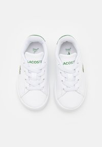 Sneaker bianca con tomaia in sintetico liscia, punta rotonda, lacci bianchi piatti e un logo Lacoste verde sul lato. Soletta testurizzata.
