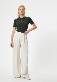 Polo shirt en tricot côtelé vert foncé à manches courtes, assorti à un pantalon large crème taille haute et à des chaussures plates beiges.