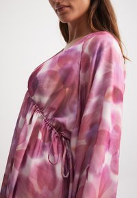 Vloeiende, roze jurk met een bloemenpatroon, met een geraffineerde taille en lange mouwen. Gemaakt van lichtgewicht, doorschijnende stof.