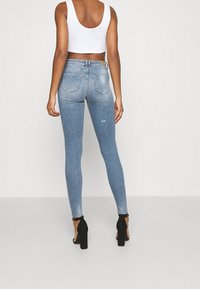 Vaqueros de denim azules ajustados con un lavado deslavado, que presentan un ligero desgaste y dos bolsillos traseros, combinados con sandalias negras de tacón alto.