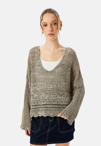Lichtgewicht gebreid vest in gedempt beige met een v-hals, lange mouwen en textuurpatronen, gecombineerd met een donkere spijkerrok.
