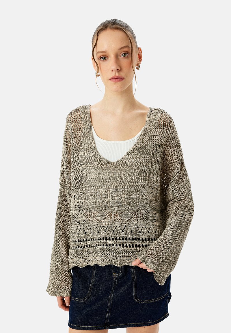 Lichtgewicht gebreid vest in gedempt beige met een v-hals, lange mouwen en textuurpatronen, gecombineerd met een donkere spijkerrok.