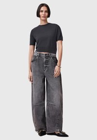 Mørkegrå cropped t-shirt parret med vide, slidte grå jeans. Fodtøj er sorte, spidse loafers. Enkel design, afslappet look.
