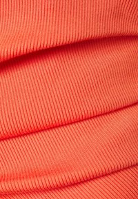 Tejido acanalado en un brillante color coral, con franjas anchas y estrechas alternadas, y una superficie suave y texturizada. Colgado en pliegues.