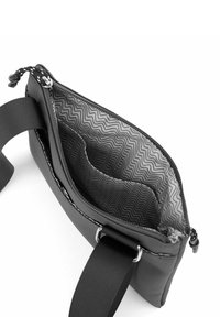 Černá syntetická taška se zipem nahoře, s vlnitým vzorem uvnitř a pevným popruhem. Viditelný malý vnitřní oddíl.