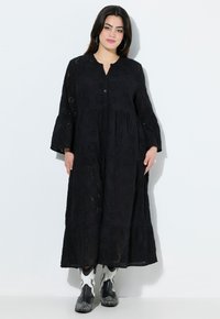 Musta, pitkähihainen mekko, jossa on silkkipistokirjontaa, V-pääntie, nappisuljenta, kerroksellinen hame ja laskeutuva siluetti. Yhdistetty mustavalkoisiin saappaisiin.