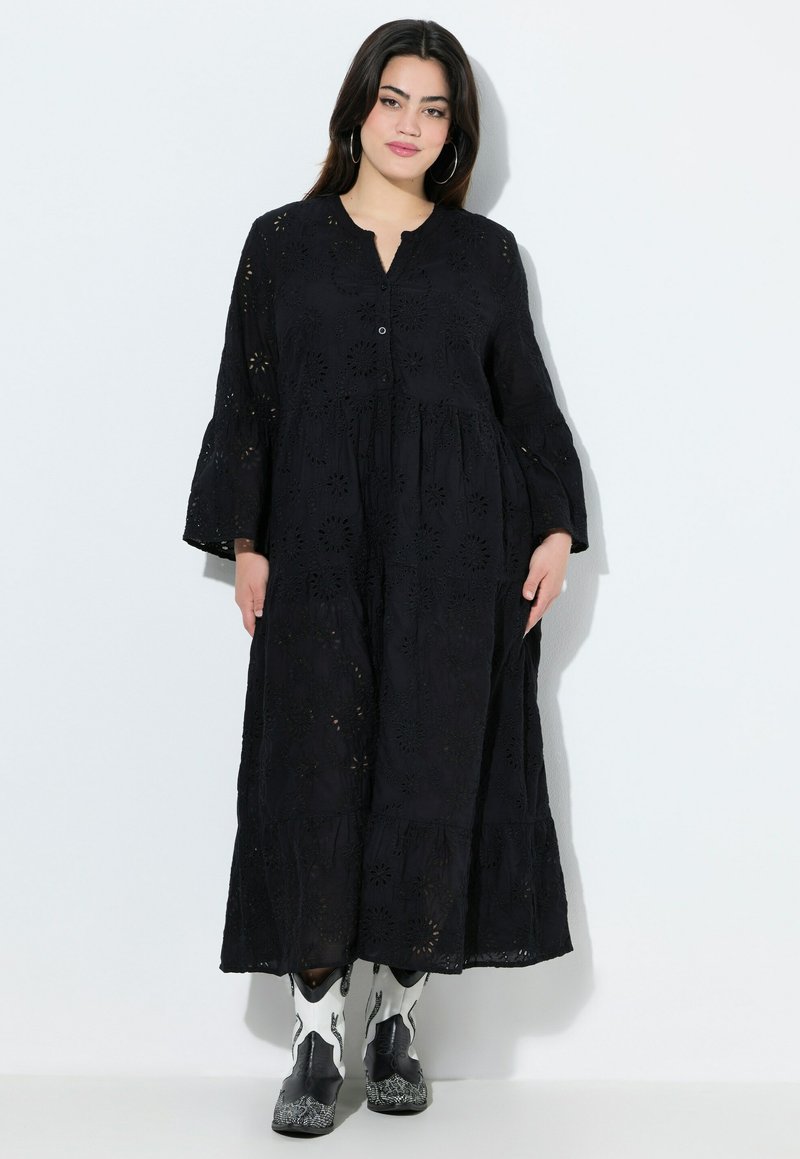 Musta, pitkähihainen mekko, jossa on silkkipistokirjontaa, V-pääntie, nappisuljenta, kerroksellinen hame ja laskeutuva siluetti. Yhdistetty mustavalkoisiin saappaisiin.