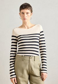 T-shirt de manga longa com riscas pretas e bege, com um decote barco, combinada com calças de cintura alta em verde oliva com bolsos frontais.