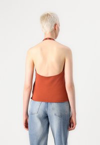 Un top halter couleur rouille en tissu doux, avec une silhouette ajustée et un dos nu, associé à un jean taille haute bleu clair.