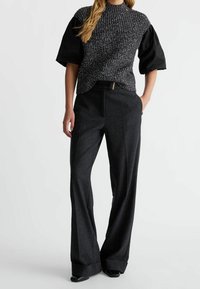 Pletený černošedý top s krátkými nabíranými rukávy, doplněný o vysokým pasem rozšířené tmavě šedé kalhoty s předním zipem a kapsami.