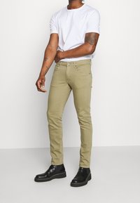 Beige slim-fit jeans i bomull, med en klassisk femficksdesign och subtila sömnadsdetaljer, matchade med svarta ankelskor.
