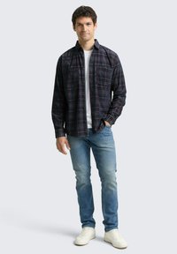 Flanellen overhemd in marineblauw met rood geruit patroon, lange mouwen, twee borstzakken; gecombineerd met lichtblauwe spijkerbroek en witte sneakers.