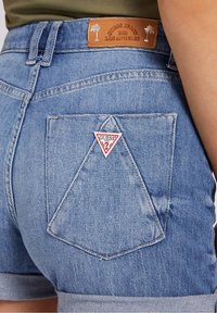Jasnoniebieskie szorty dżinsowe z podwiniętym dołem, z trójkątną tylną kieszenią i skórzaną metką z tłoczeniem "GUESS JEANS 1981 LOS ANGELES".
