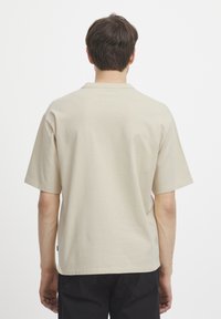 Beige bomulls t-skjorte med korte ermer, rund hals og avslappet passform. Har minimal søm og et lite logomerke på siden.